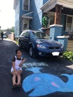 一位年轻的利记sbo拿着她在自家车道上画的鲸鱼照片摆姿势.