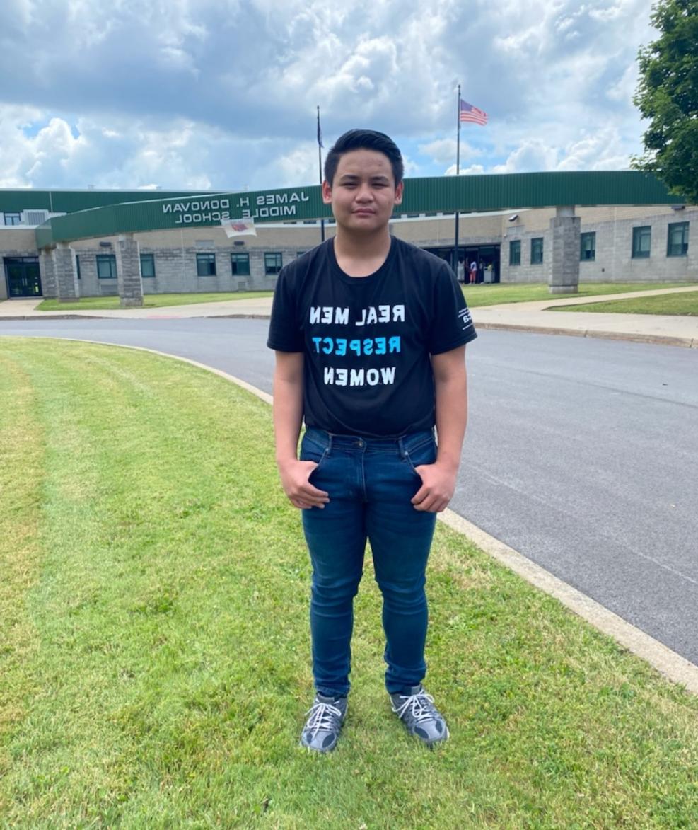 一名年轻的男学生站在多诺万中学门前，穿着一件“修正在一起”的衬衫.